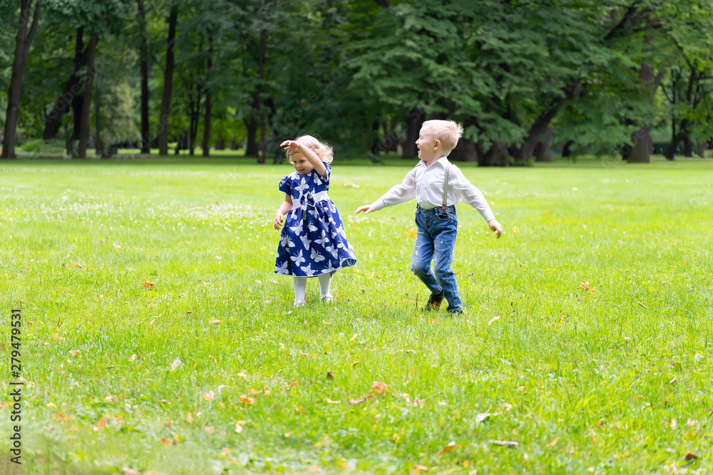 Obraz premium A boy and a girl are running around the grass, laughing and rejoicing. In the background are trees. Children are happy