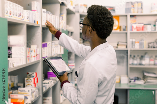 African American male pharmacist using digital tablet during inventory in pharmacy. photo