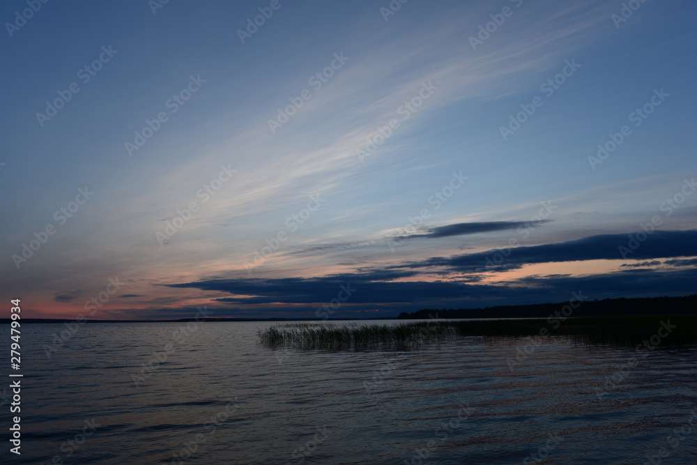 Twilight blue sky in cirrus clouds at sunset in a dark blue cloud on the horizon above the water of the lake