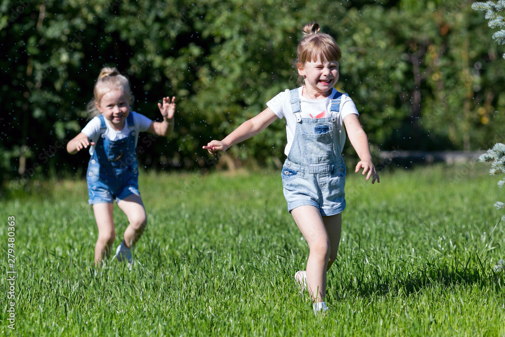 Children run on the green grass holding Girls running around the lawn with grass playing with splashes of water to water the plants