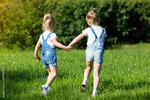 Children run on the green grass holding hands. Girls running around the lawn with grass playing with splashes of water to water the plants