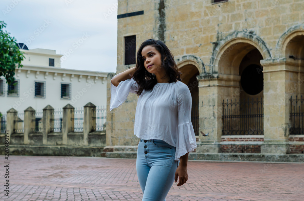 Outdoor portrait of young beautiful girl 9 to 25 years old posing in street. wearing white blouse and tight jeans and sapatillas. City lifestyle. Female fashion concept.