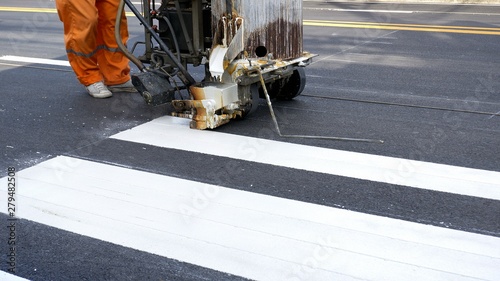 Low section of road worker with thermoplastic spray road marking machine working to paint pedestrian crosswalk on asphalt road surface in the city, construction concept