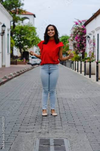 Outdoor portrait of young beautiful girl 19 to 25 years old. Brunette. posing in the middle of a colonial street with cobblestones. Wearing red blouse City lifestyle. Female fashion concept. © Francisco