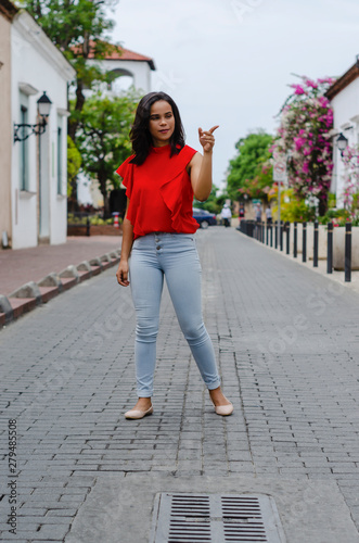 Outdoor portrait of young beautiful girl 19 to 25 years old. Brunette. posing in the middle of a colonial street with cobblestones. Wearing red blouse City lifestyle. Female fashion concept. © Francisco