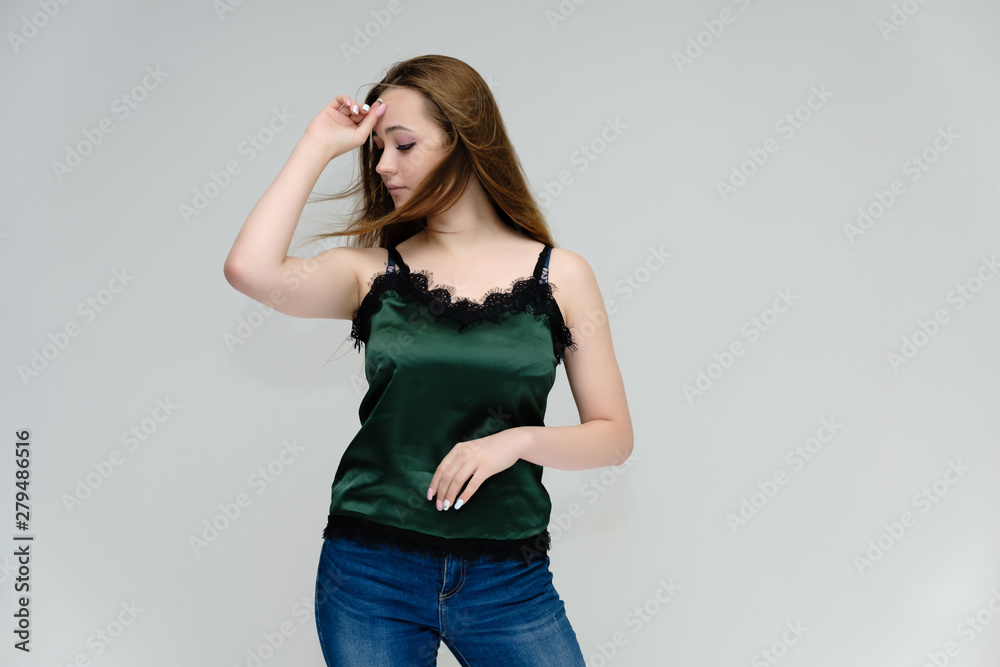 Concept portrait above the knee of a pretty girl, young woman with long beautiful brown hair in a green T-shirt and blue jeans on a white background. In the studio in different poses showing emotions.