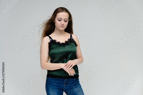 Concept portrait above the knee of a pretty girl, young woman with long beautiful brown hair in a green T-shirt and blue jeans on a white background. In the studio in different poses showing emotions.