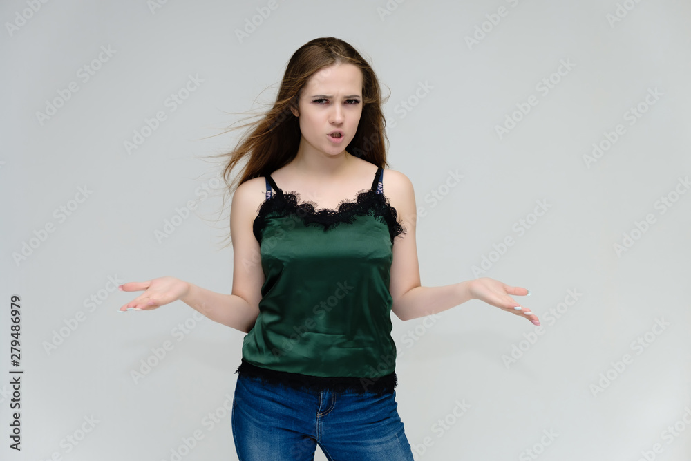 Concept portrait above the knee of a pretty girl, young woman with long beautiful brown hair in a green T-shirt and blue jeans on a white background. In the studio in different poses showing emotions. Concept portrait above the knee of a pretty girl, young woman with long beautiful brown hair in a green T-shirt and blue jeans on a white background. In the studio in different poses showing emotions.