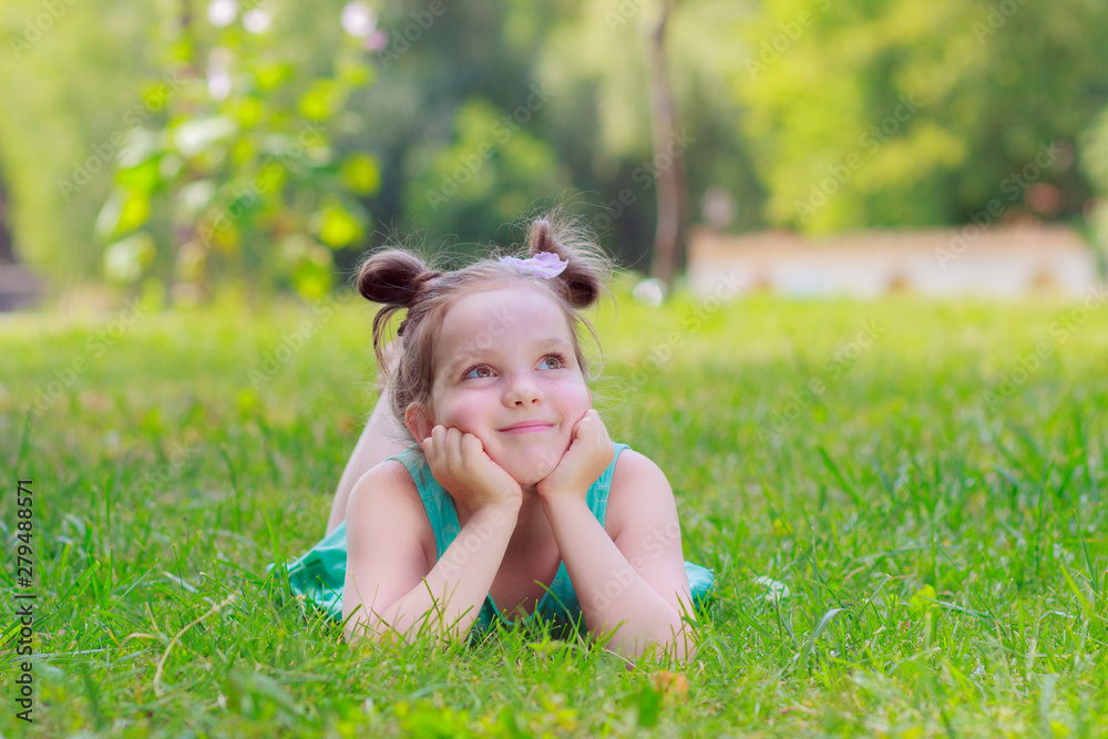 Cute girl lying on the green grass, outdoors, summer time, blurred background Cute girl lying on the green grass, outdoors, summer time, blurred background