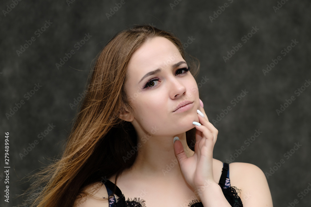 Concept close-up portrait of a pretty girl, young woman with long beautiful brown hair and beautiful face skin on a gray background. In the studio in different poses showing emotions.