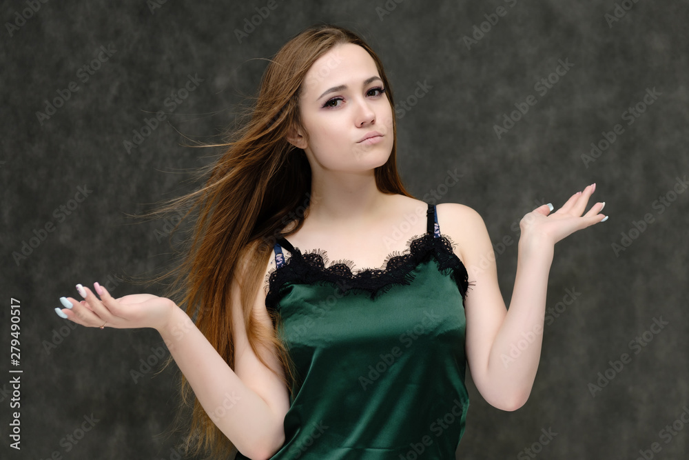 Concept portrait of the waist of a pretty girl, a young woman with long beautiful brown hair and a green T-shirt on a gray background. In the studio in different poses showing emotions. Concept portrait of the waist of a pretty girl, a young woman with long beautiful brown hair and a green T-shirt on a gray background. In the studio in different poses showing emotions.