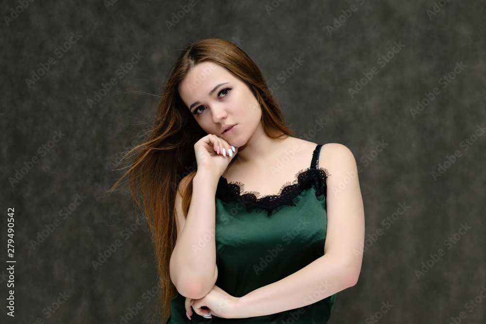 Concept portrait of the waist of a pretty girl, a young woman with long beautiful brown hair and a green T-shirt on a gray background. In the studio in different poses showing emotions. Concept portrait of the waist of a pretty girl, a young woman with long beautiful brown hair and a green T-shirt on a gray background. In the studio in different poses showing emotions.