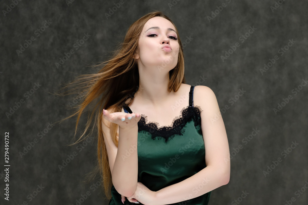 Concept portrait of the waist of a pretty girl, a young woman with long beautiful brown hair and a green T-shirt on a gray background. In the studio in different poses showing emotions. Concept portrait of the waist of a pretty girl, a young woman with long beautiful brown hair and a green T-shirt on a gray background. In the studio in different poses showing emotions.