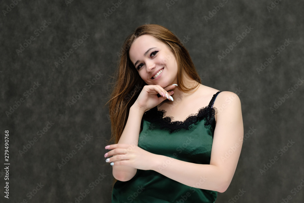 Concept portrait of the waist of a pretty girl, a young woman with long beautiful brown hair and a green T-shirt on a gray background. In the studio in different poses showing emotions. Concept portrait of the waist of a pretty girl, a young woman with long beautiful brown hair and a green T-shirt on a gray background. In the studio in different poses showing emotions.