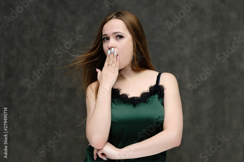 Concept portrait of the waist of a pretty girl, a young woman with long beautiful brown hair and a green T-shirt on a gray background. In the studio in different poses showing emotions.