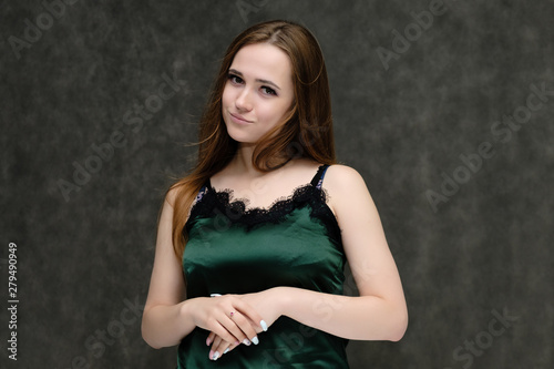 Concept portrait of the waist of a pretty girl, a young woman with long beautiful brown hair and a green T-shirt on a gray background. In the studio in different poses showing emotions.