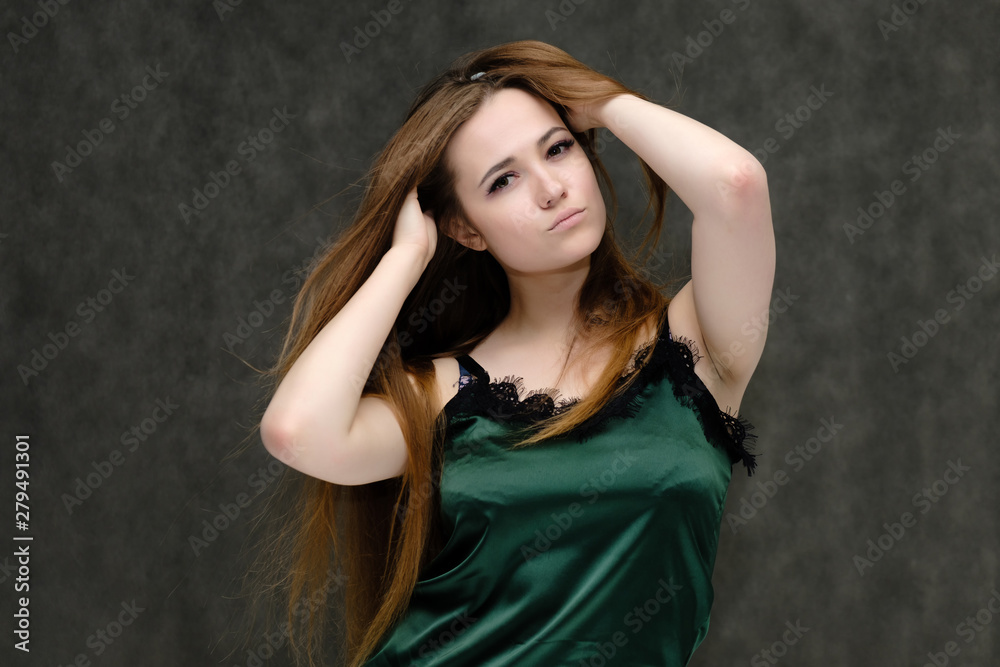 Concept portrait of the waist of a pretty girl, a young woman with long beautiful brown hair and a green T-shirt on a gray background. In the studio in different poses showing emotions. Concept portrait of the waist of a pretty girl, a young woman with long beautiful brown hair and a green T-shirt on a gray background. In the studio in different poses showing emotions.