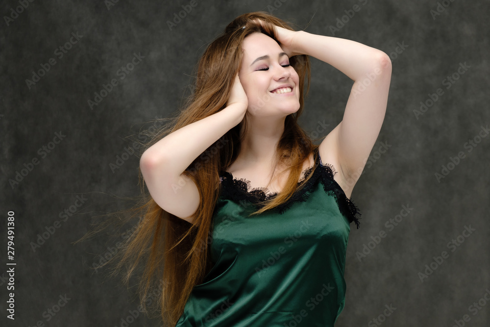 Concept portrait of the waist of a pretty girl, a young woman with long beautiful brown hair and a green T-shirt on a gray background. In the studio in different poses showing emotions.