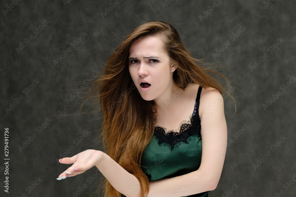 Concept portrait of the waist of a pretty girl, a young woman with long beautiful brown hair and a green T-shirt on a gray background. In the studio in different poses showing emotions.