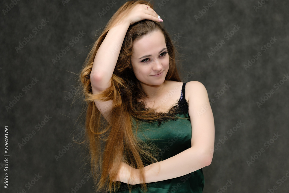 Concept portrait of the waist of a pretty girl, a young woman with long beautiful brown hair and a green T-shirt on a gray background. In the studio in different poses showing emotions. Concept portrait of the waist of a pretty girl, a young woman with long beautiful brown hair and a green T-shirt on a gray background. In the studio in different poses showing emotions.