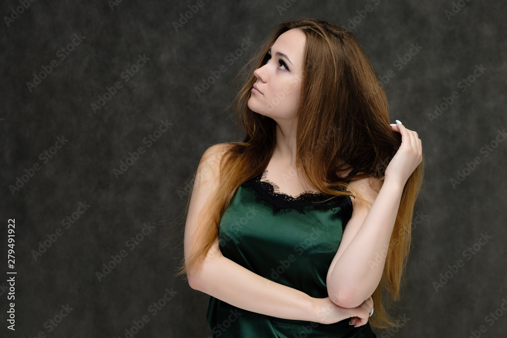 Concept portrait of the waist of a pretty girl, a young woman with long beautiful brown hair and a green T-shirt on a gray background. In the studio in different poses showing emotions. Concept portrait of the waist of a pretty girl, a young woman with long beautiful brown hair and a green T-shirt on a gray background. In the studio in different poses showing emotions.