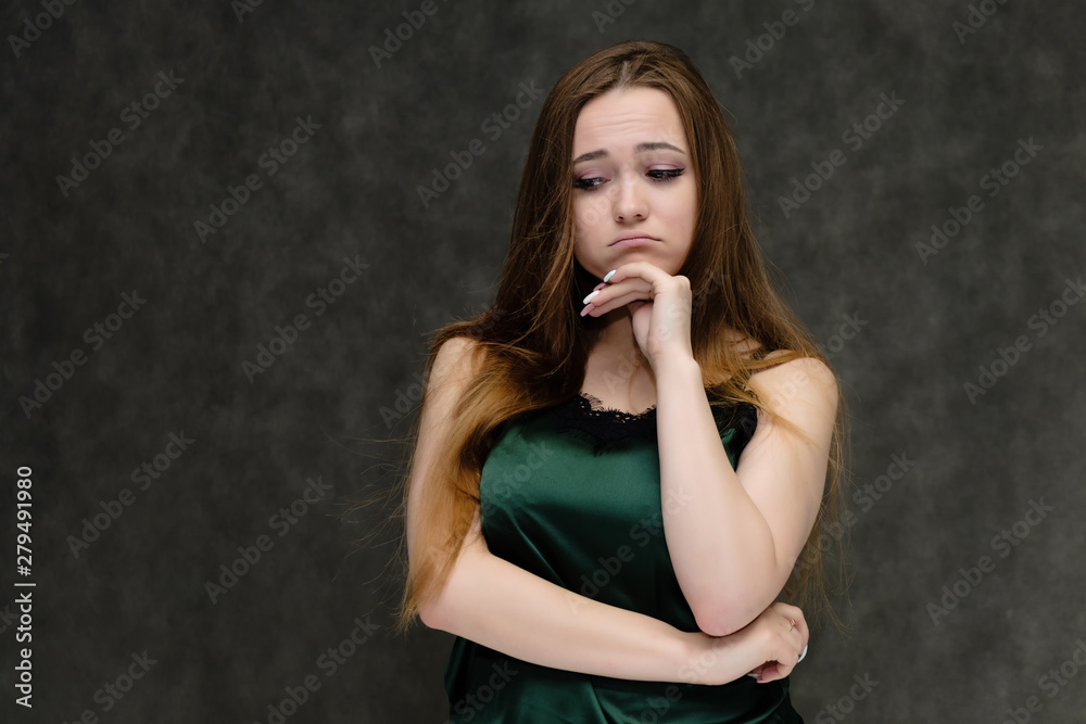 Concept portrait of the waist of a pretty girl, a young woman with long beautiful brown hair and a green T-shirt on a gray background. In the studio in different poses showing emotions. Concept portrait of the waist of a pretty girl, a young woman with long beautiful brown hair and a green T-shirt on a gray background. In the studio in different poses showing emotions.