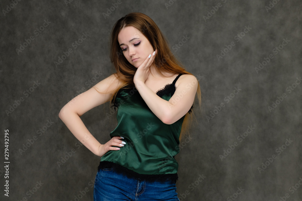 Concept portrait below belt of pretty girl, young woman with long beautiful brown hair and green t-shirt and blue jeans on gray background. In the studio in different poses showing emotions.