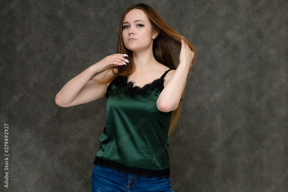 Concept portrait below belt of pretty girl, young woman with long beautiful brown hair and green t-shirt and blue jeans on gray background. In the studio in different poses showing emotions. Concept portrait below belt of pretty girl, young woman with long beautiful brown hair and green t-shirt and blue jeans on gray background. In the studio in different poses showing emotions.