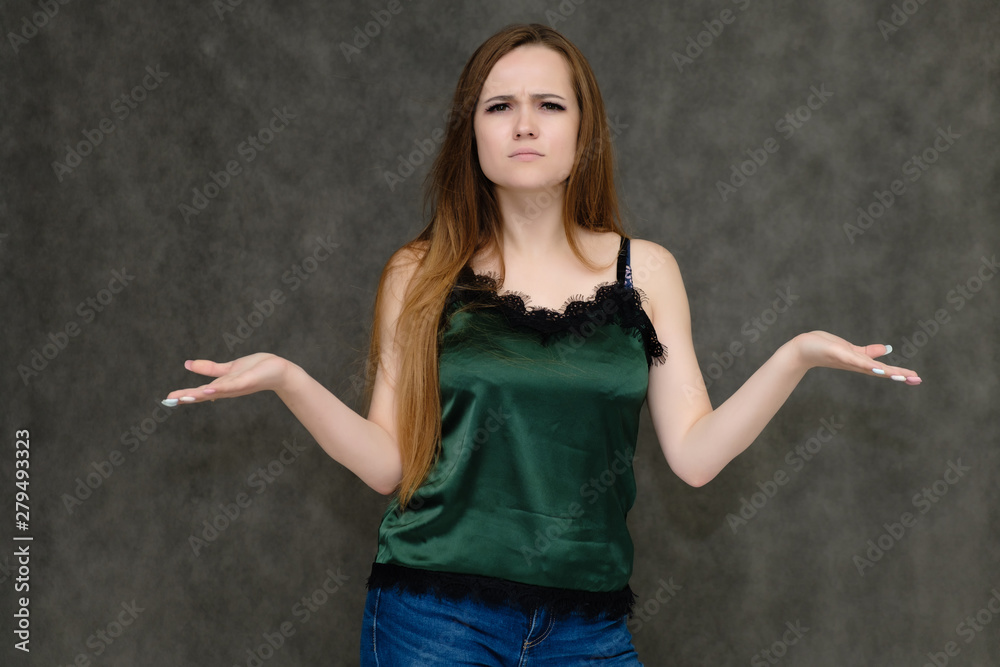 Concept portrait below belt of pretty girl, young woman with long beautiful brown hair and green t-shirt and blue jeans on gray background. In the studio in different poses showing emotions. Concept portrait below belt of pretty girl, young woman with long beautiful brown hair and green t-shirt and blue jeans on gray background. In the studio in different poses showing emotions.