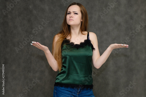 Concept portrait below belt of pretty girl, young woman with long beautiful brown hair and green t-shirt and blue jeans on gray background. In the studio in different poses showing emotions.