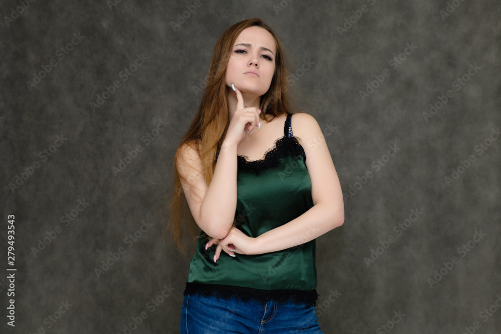Concept portrait below belt of pretty girl, young woman with long beautiful brown hair and green t-shirt and blue jeans on gray background. In the studio in different poses showing emotions. Concept portrait below belt of pretty girl, young woman with long beautiful brown hair and green t-shirt and blue jeans on gray background. In the studio in different poses showing emotions.