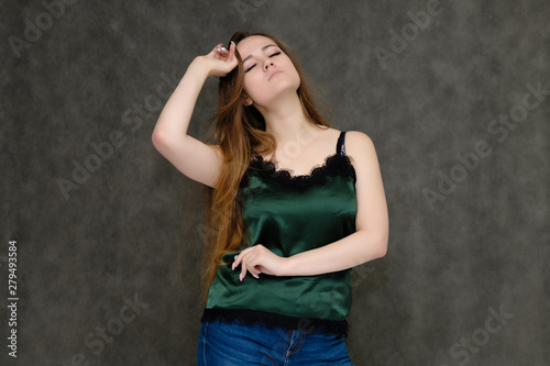 Concept portrait below belt of pretty girl, young woman with long beautiful brown hair and green t-shirt and blue jeans on gray background. In the studio in different poses showing emotions. © Вячеслав Чичаев
