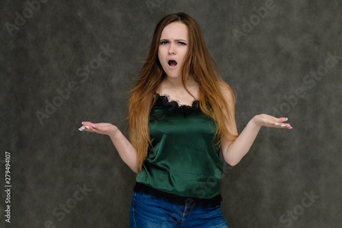 Concept portrait below belt of pretty girl, young woman with long beautiful brown hair and green t-shirt and blue jeans on gray background. In the studio in different poses showing emotions.