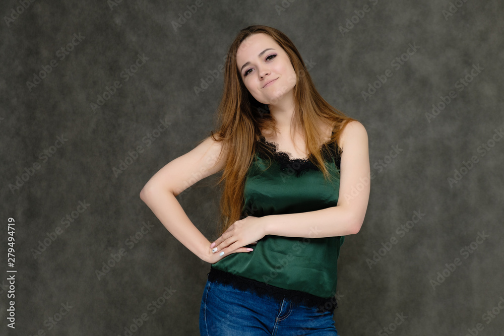 Concept portrait below belt of pretty girl, young woman with long beautiful brown hair and green t-shirt and blue jeans on gray background. In the studio in different poses showing emotions. Concept portrait below belt of pretty girl, young woman with long beautiful brown hair and green t-shirt and blue jeans on gray background. In the studio in different poses showing emotions.
