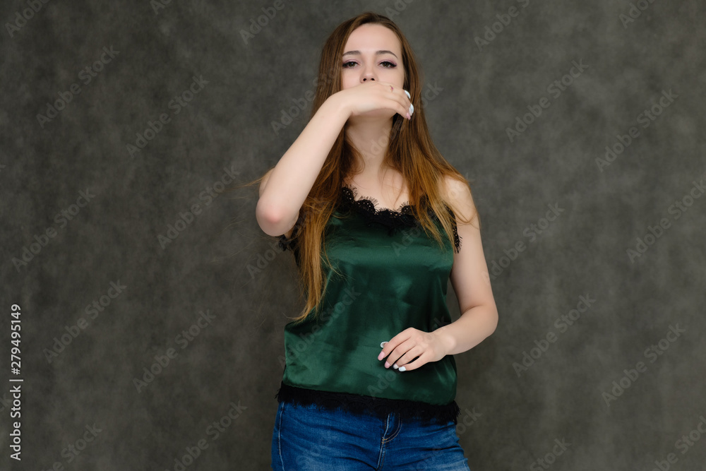 Concept portrait below belt of pretty girl, young woman with long beautiful brown hair and green t-shirt and blue jeans on gray background. In the studio in different poses showing emotions.