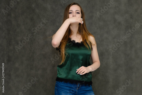 Concept portrait below belt of pretty girl, young woman with long beautiful brown hair and green t-shirt and blue jeans on gray background. In the studio in different poses showing emotions. © Вячеслав Чичаев