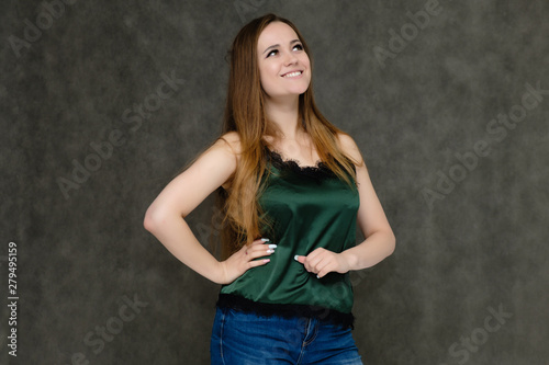 Concept portrait below belt of pretty girl, young woman with long beautiful brown hair and green t-shirt and blue jeans on gray background. In the studio in different poses showing emotions. © Вячеслав Чичаев