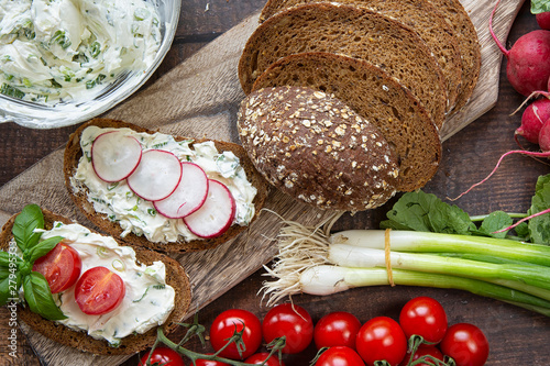 Preparation of summer sandwiches cottage cheese with green onions, radishes and tomatoes. keto diet ,healthy lifestyle. fresh fruit.On a dark background .wood boards