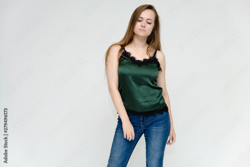 Concept portrait above the knee of a pretty girl, a young woman with long beautiful brown hair and a green t-shirt and blue jeans on a white background. In studio in different poses showing emotions. Concept portrait above the knee of a pretty girl, a young woman with long beautiful brown hair and a green t-shirt and blue jeans on a white background. In studio in different poses showing emotions.