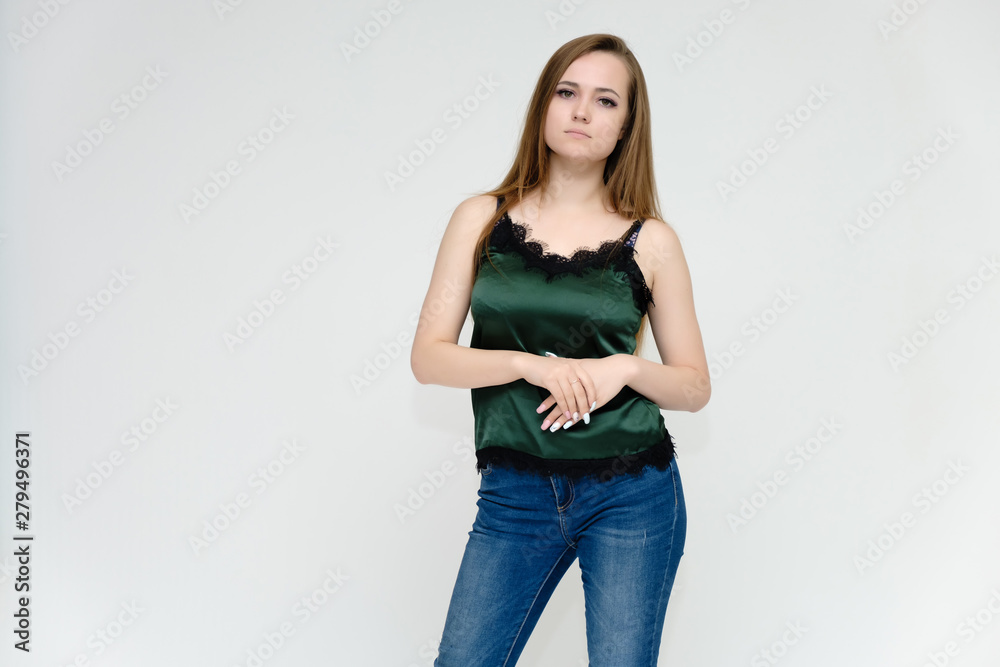 Concept portrait above the knee of a pretty girl, a young woman with long beautiful brown hair and a green t-shirt and blue jeans on a white background. In studio in different poses showing emotions. Concept portrait above the knee of a pretty girl, a young woman with long beautiful brown hair and a green t-shirt and blue jeans on a white background. In studio in different poses showing emotions.