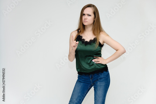 Concept portrait above the knee of a pretty girl, a young woman with long beautiful brown hair and a green t-shirt and blue jeans on a white background. In studio in different poses showing emotions.