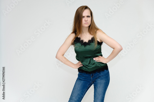 Concept portrait above the knee of a pretty girl, a young woman with long beautiful brown hair and a green t-shirt and blue jeans on a white background. In studio in different poses showing emotions.