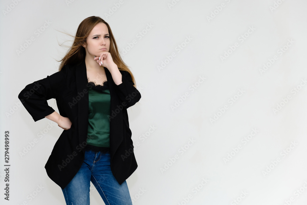 Concept portrait above the knee of a pretty girl, a young woman with long beautiful brown hair and a black jacket and blue jeans on a white background. In studio in different poses showing emotions. Concept portrait above the knee of a pretty girl, a young woman with long beautiful brown hair and a black jacket and blue jeans on a white background. In studio in different poses showing emotions.