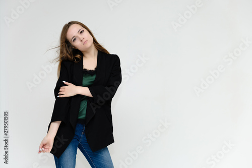 Concept portrait above the knee of a pretty girl, a young woman with long beautiful brown hair and a black jacket and blue jeans on a white background. In studio in different poses showing emotions.
