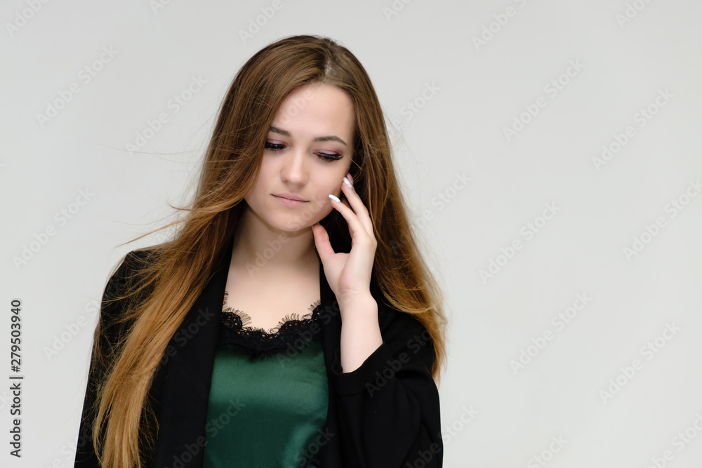 Concept close-up portrait of a pretty girl, a young woman with long beautiful brown hair and a black jacket on a white background. In the studio in different poses showing emotions. Concept close-up portrait of a pretty girl, a young woman with long beautiful brown hair and a black jacket on a white background. In the studio in different poses showing emotions.
