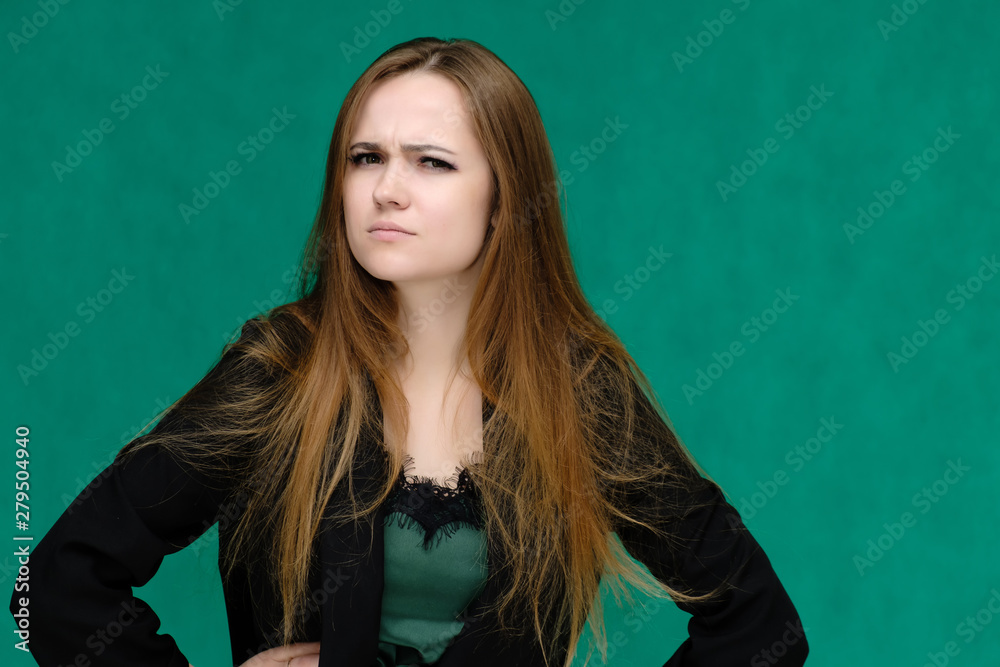 Concept close-up portrait of a pretty girl, a young woman with long beautiful brown hair and in a black jacket on a green background. In the studio in different poses showing emotions. Concept close-up portrait of a pretty girl, a young woman with long beautiful brown hair and in a black jacket on a green background. In the studio in different poses showing emotions.