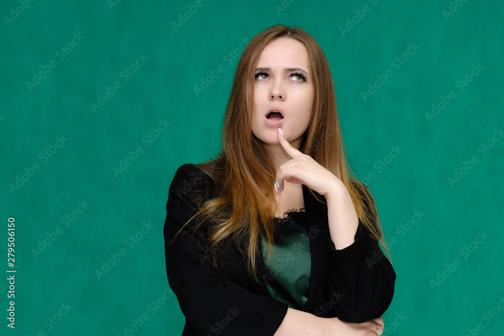 Concept close-up portrait of a pretty girl, a young woman with long beautiful brown hair and in a black jacket on a green background. In the studio in different poses showing emotions. Concept close-up portrait of a pretty girl, a young woman with long beautiful brown hair and in a black jacket on a green background. In the studio in different poses showing emotions.
