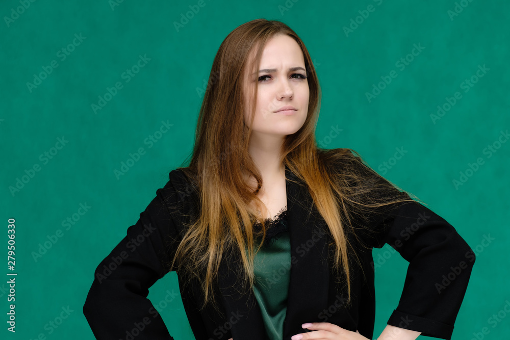 Concept close-up portrait of a pretty girl, a young woman with long beautiful brown hair and in a black jacket on a green background. In the studio in different poses showing emotions. Concept close-up portrait of a pretty girl, a young woman with long beautiful brown hair and in a black jacket on a green background. In the studio in different poses showing emotions.