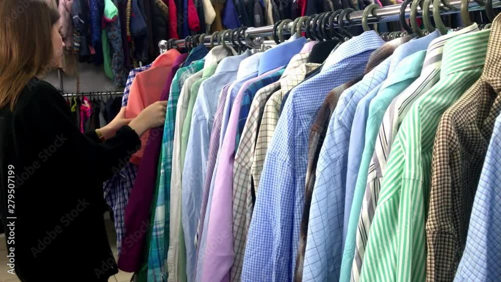Closeup hand woman in the shop looks through jackets and shirts, which are hanging on the racks Closeup hand woman in the shop looks through jackets and shirts, which are hanging on the racks
