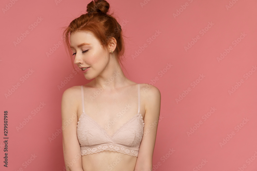 Young red-haired woman wearing lace bra with a bun on her head poses tilting her head to one side Young red-haired woman wearing lace bra with a bun on her head poses tilting her head to one side